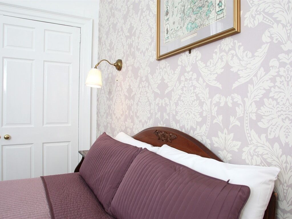 A bedroom with a bed, a wall-mounted lamp, and a framed picture.