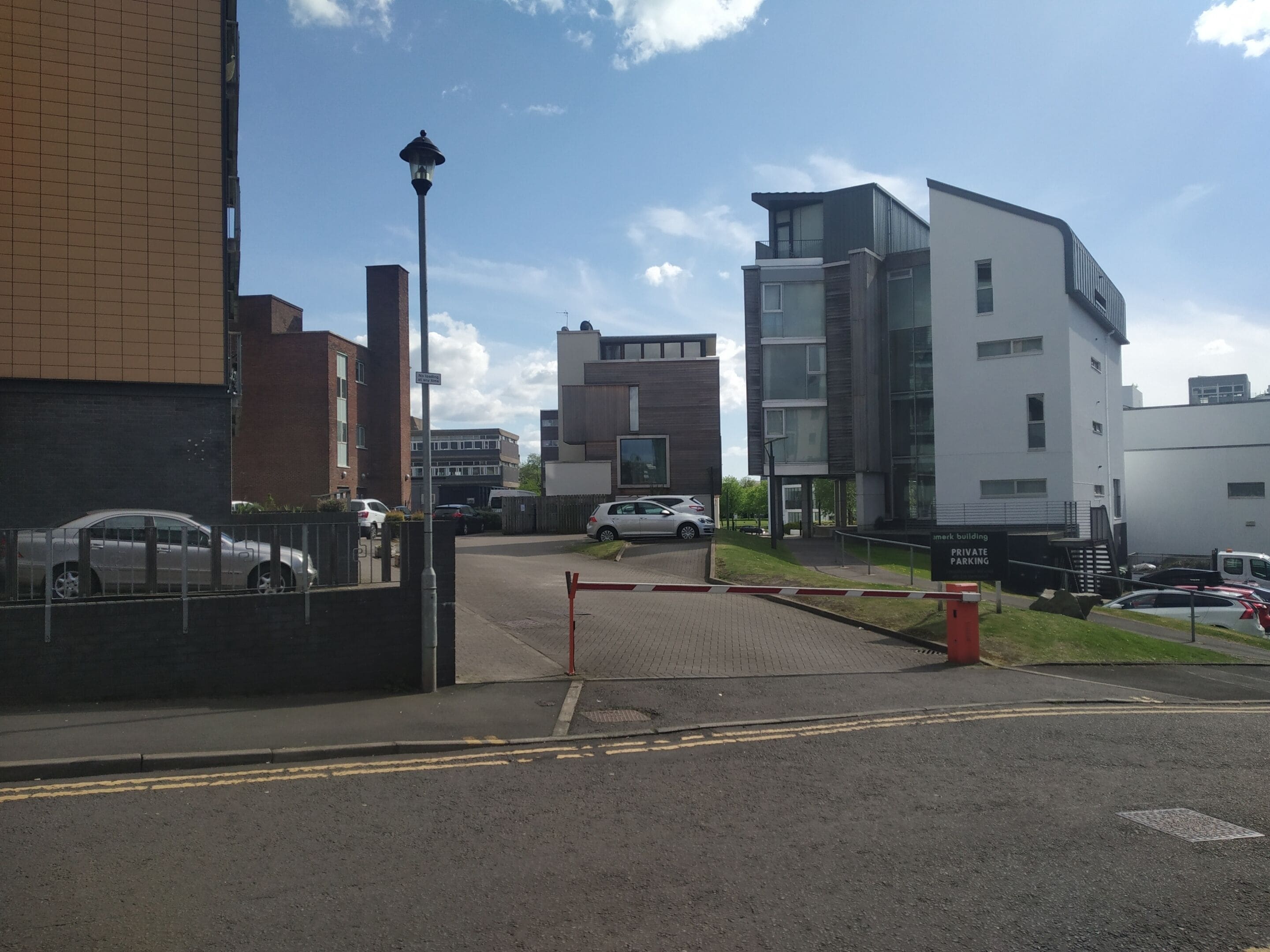 A modern building with a gated entrance, a street with parked cars, and a clear sky.