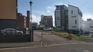 A modern building with a gated entrance, a street with parked cars, and a clear sky.
