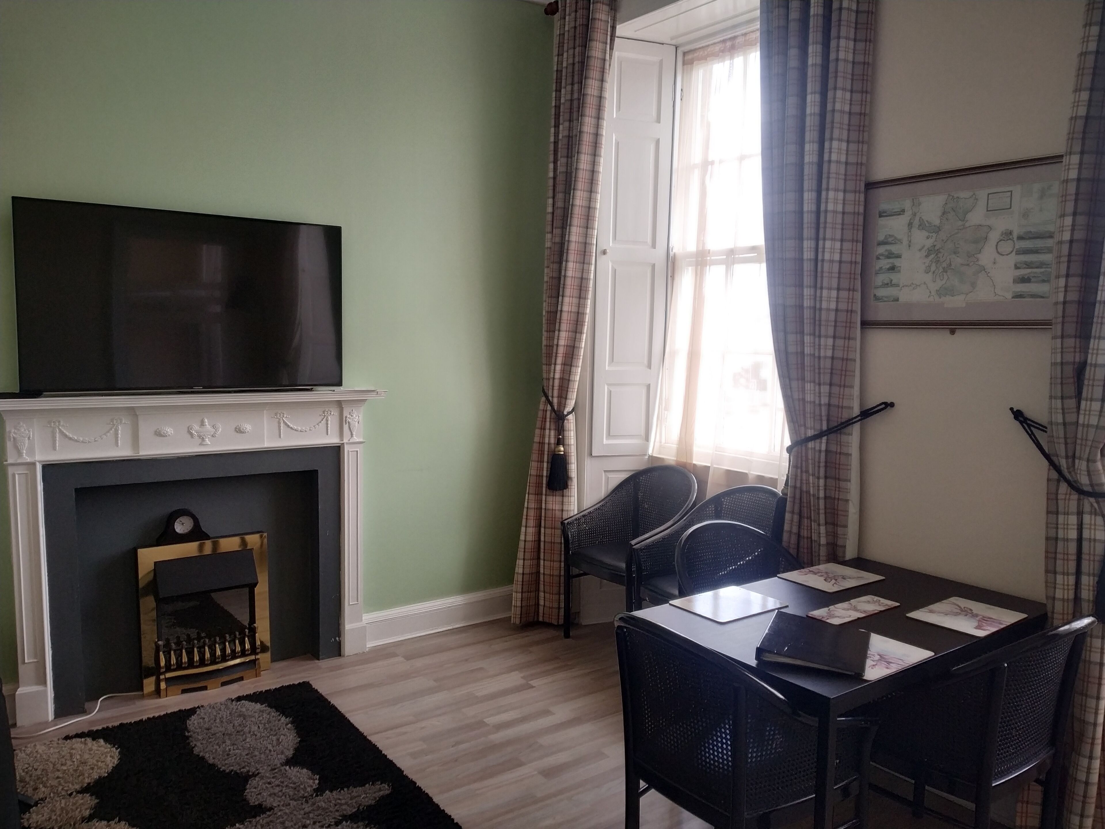 Een kamer met een open haard, een televisie erboven, een eettafel met stoelen en een raam met gordijnen.