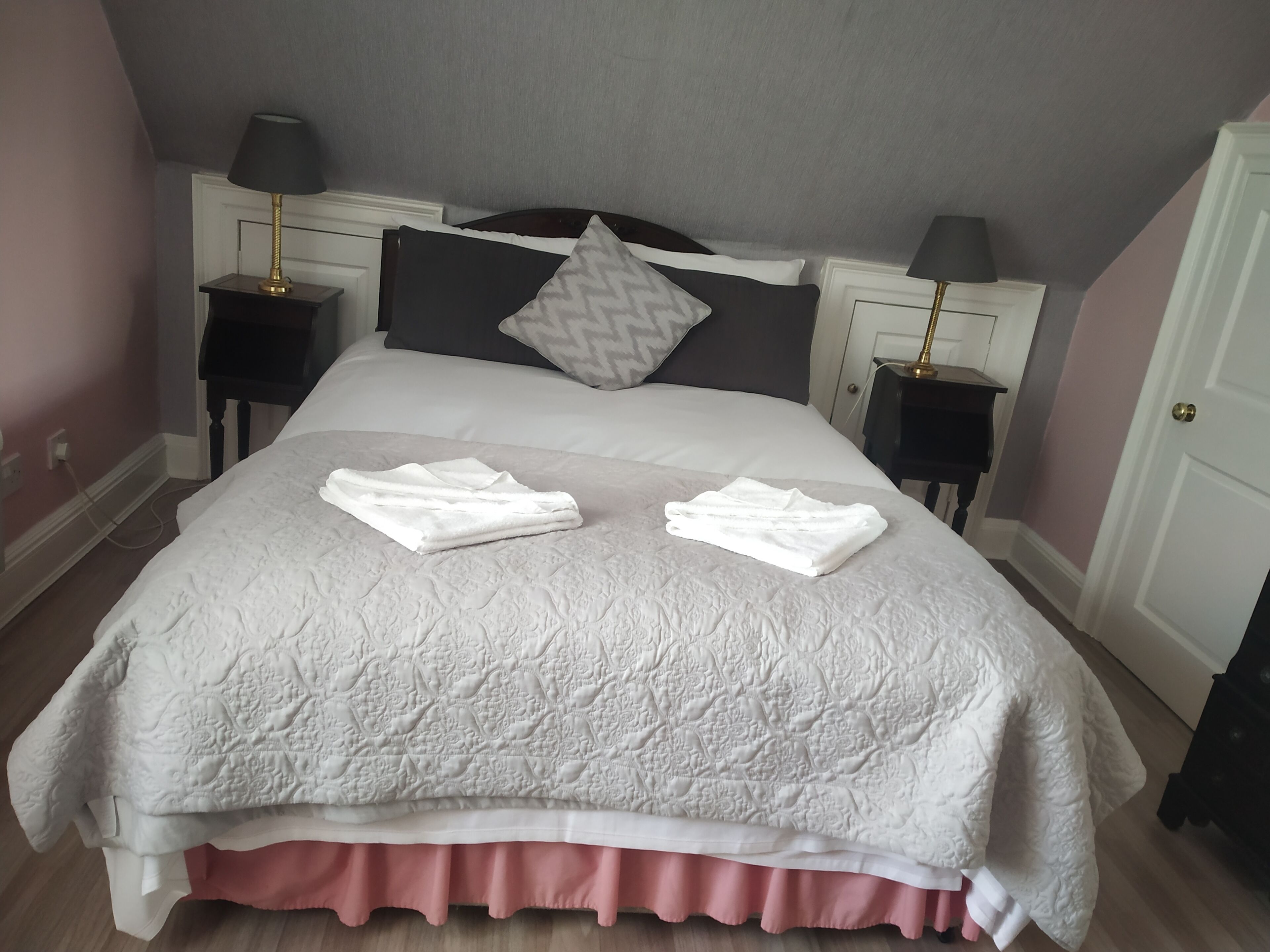 A neatly made bed with a white quilt, two folded towels, and a pink skirt at the foot.
