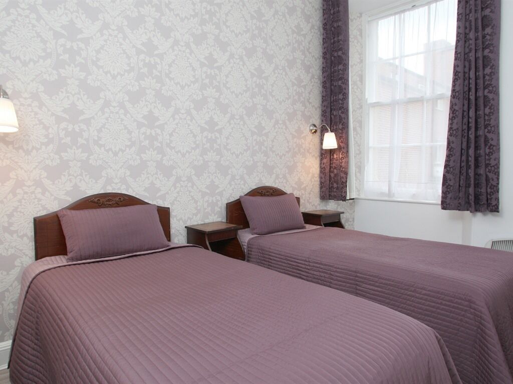 A hotel room with two beds, a window with curtains, and a wall with a floral pattern.