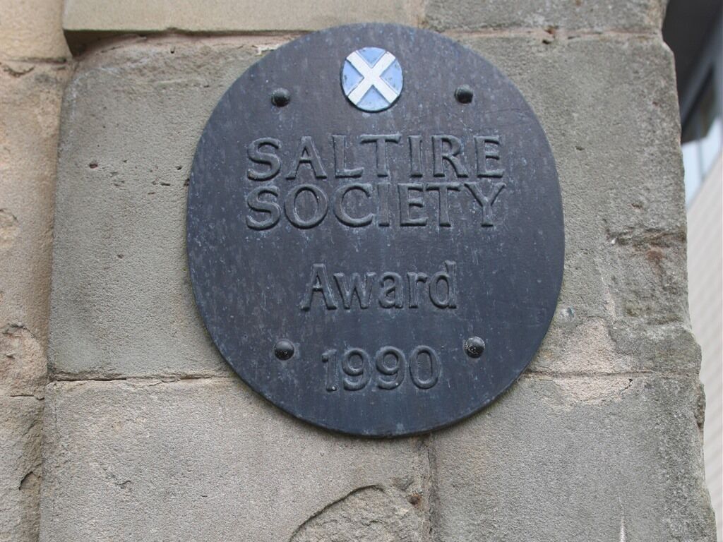 Een plaquette op een stenen muur met de tekst 'SALTIRE SOCIETY Award 1990'.