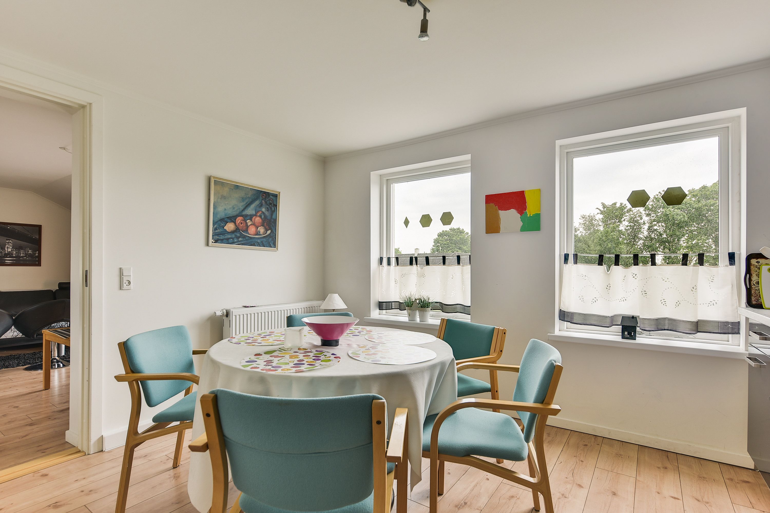 A dining area with a round table, teal chairs, and a white tablecloth.