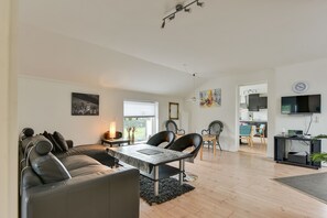 A modern living room with a sofa, dining table, and chairs. There is a kitchen area visible in the background. - Bjerndrup Apartments (Aabenraa)