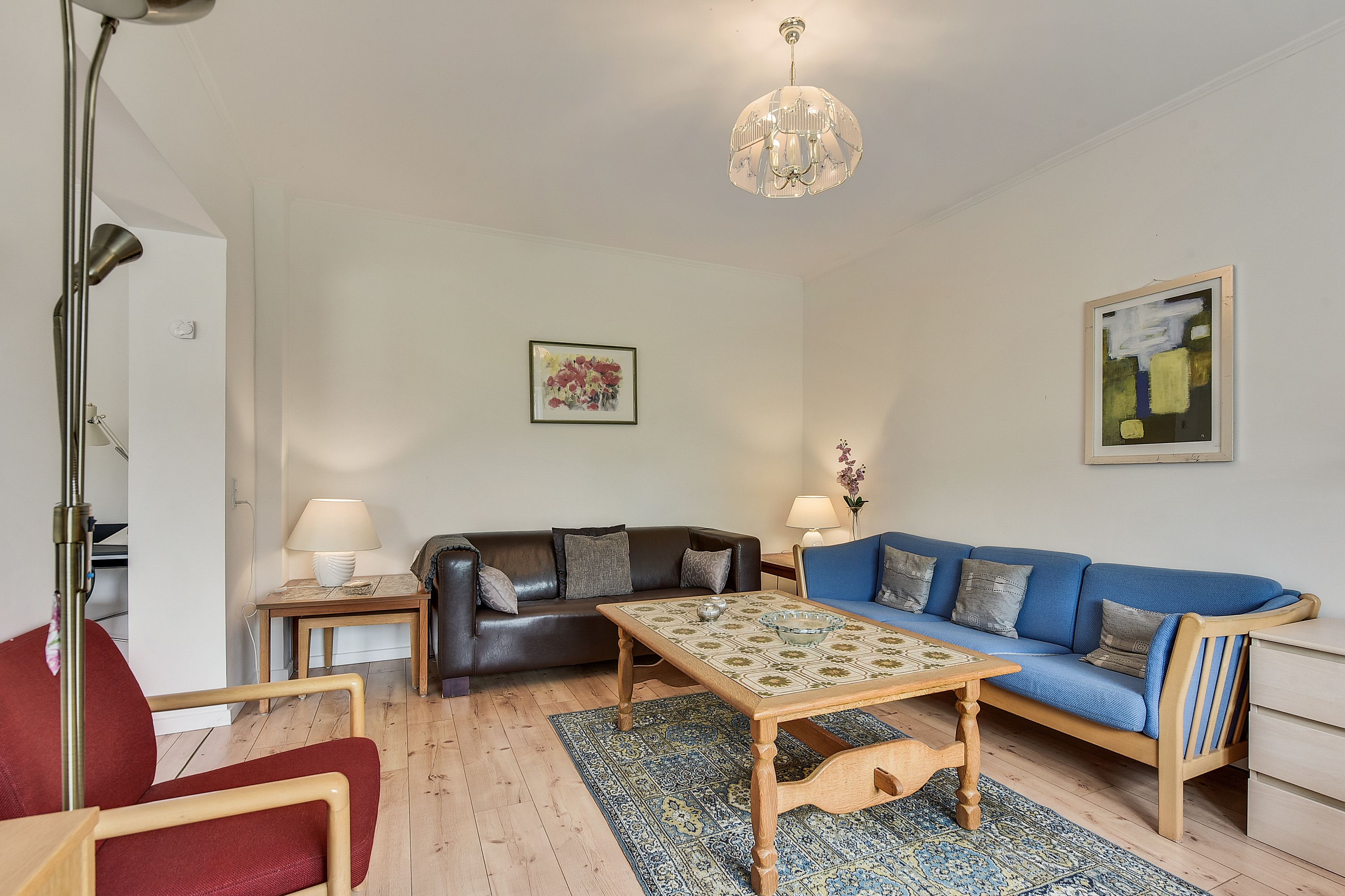 A living room with a wooden coffee table, a blue sofa, a red chair, and a black leather couch.