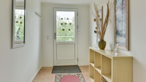 A hallway with a white door, a small window, and a wooden console table with a vase and a glass. - Bjerndrup Apartments (Aabenraa)