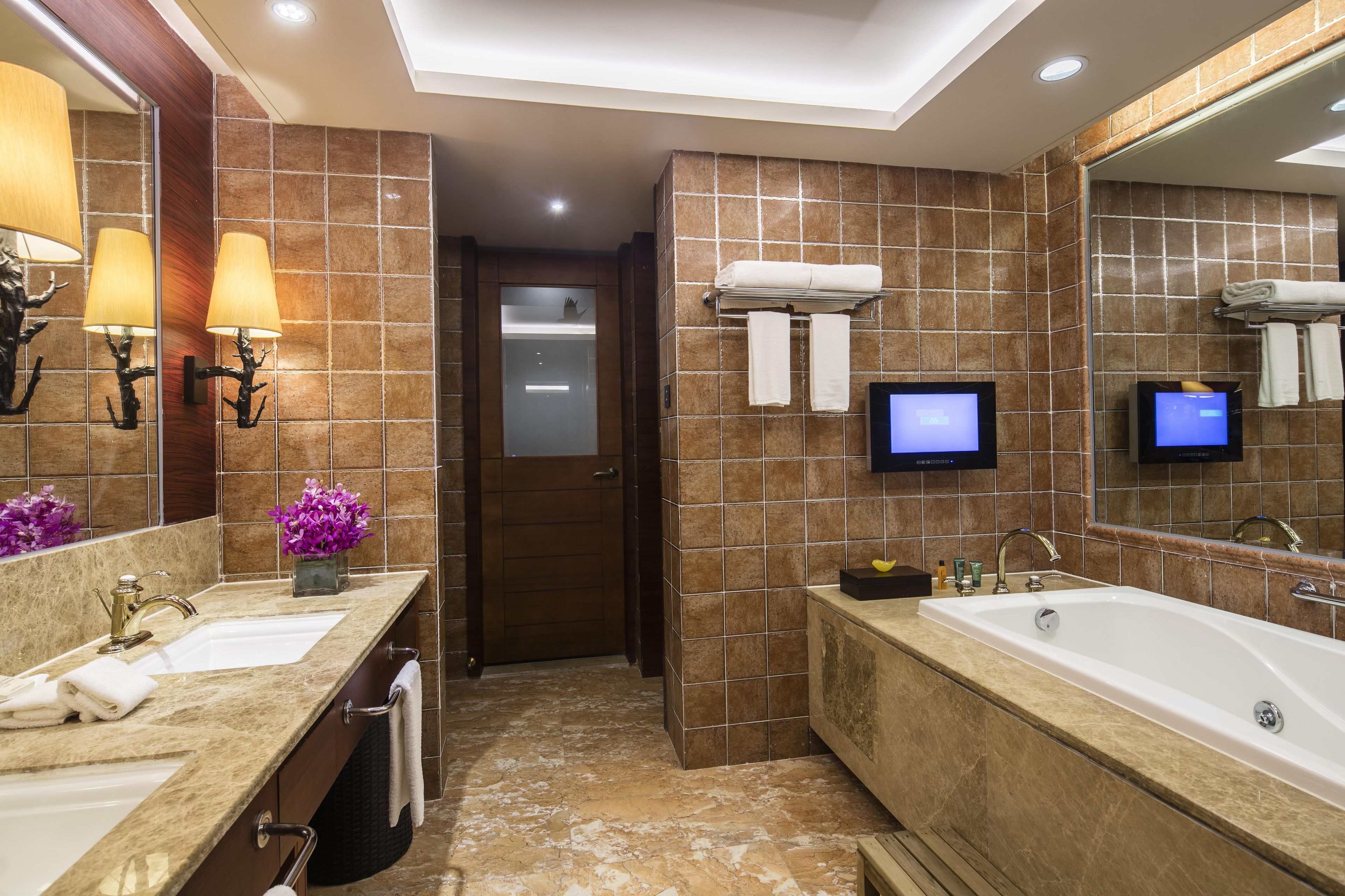 Un baño moderno con dos lavamanos, una bañera grande y un televisor de pantalla plana montado en la pared.