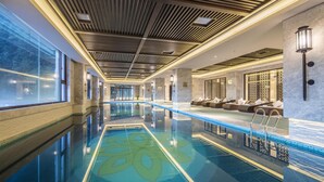 Piscina interior moderna com padrão geométrico de azulejos, teto de madeira com ripas e área de estar com almofadas.