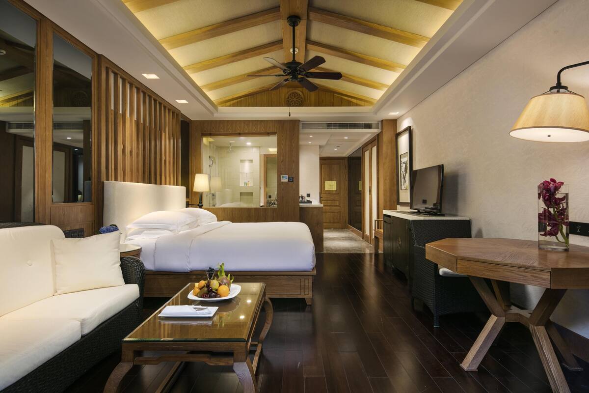 Una habitación de hotel con una cama, un sofá, una mesa de centro, un escritorio y una televisión.