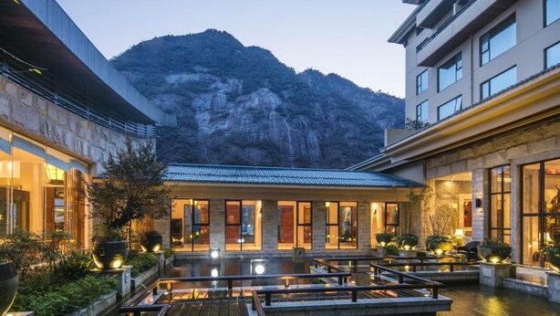 Hotel com pátio, montanhas ao fundo e um elemento aquático.