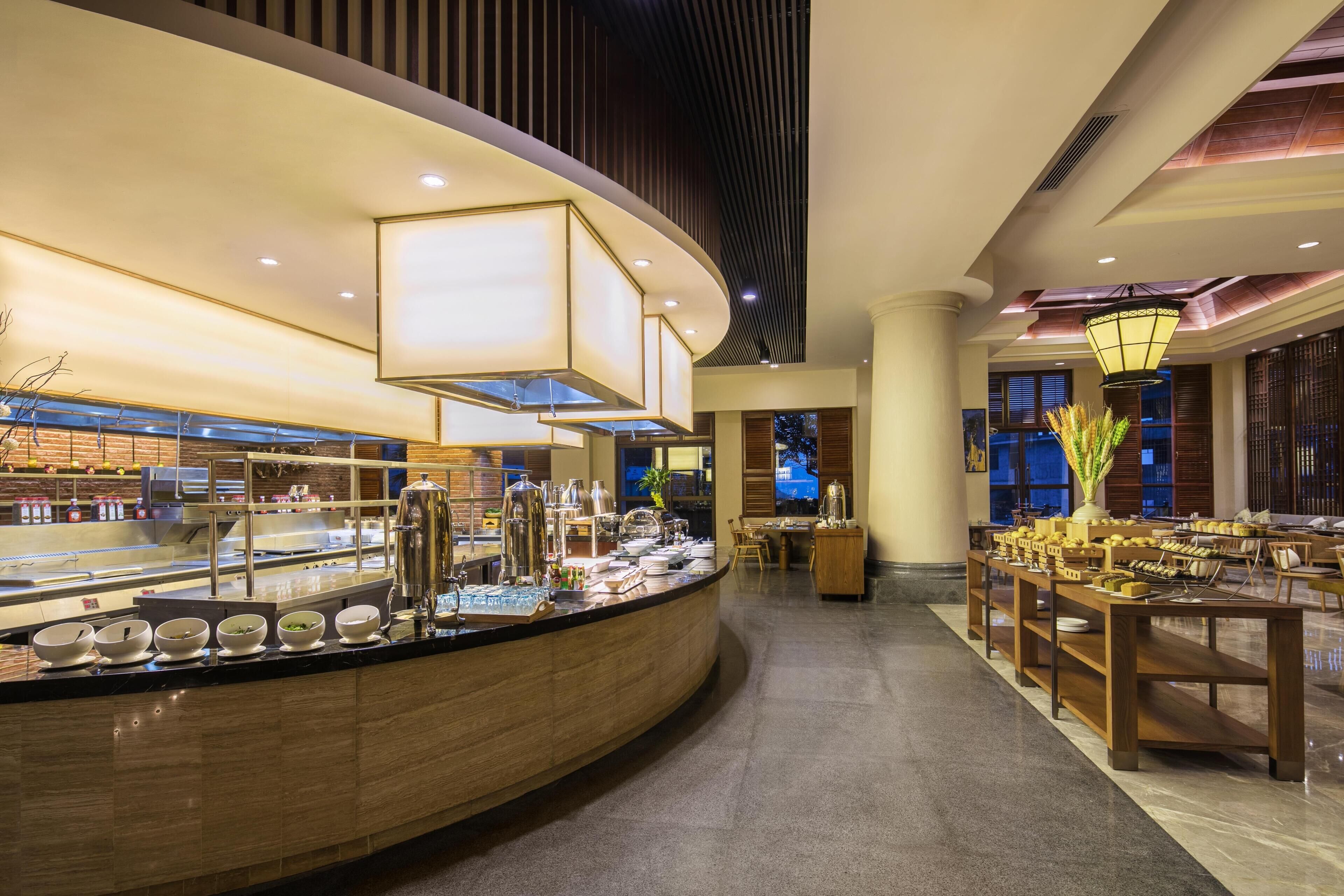 A well-lit buffet area with a curved counter, various food and drink dispensers, and seating arrangements.