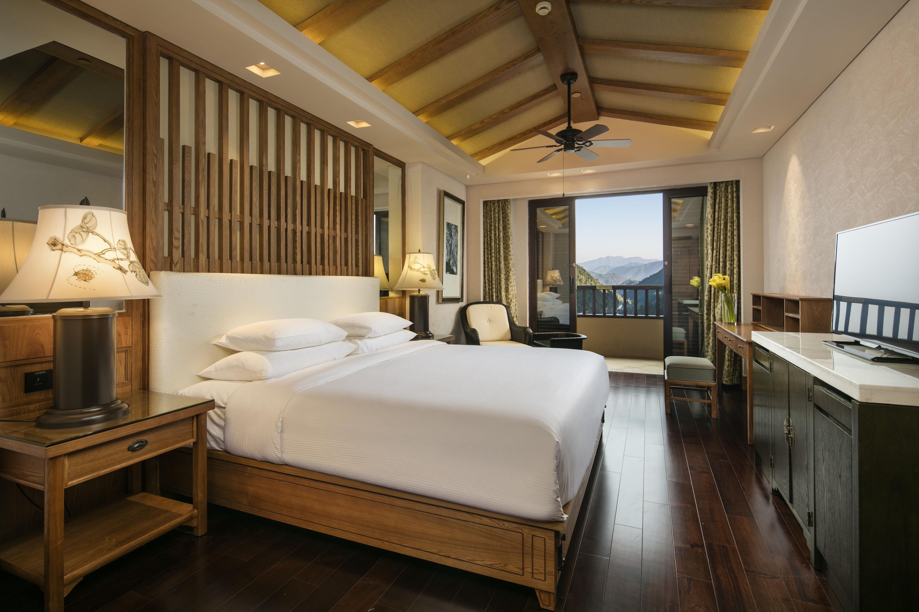 A hotel room with a large bed, a desk, a chair, and a balcony with a view.