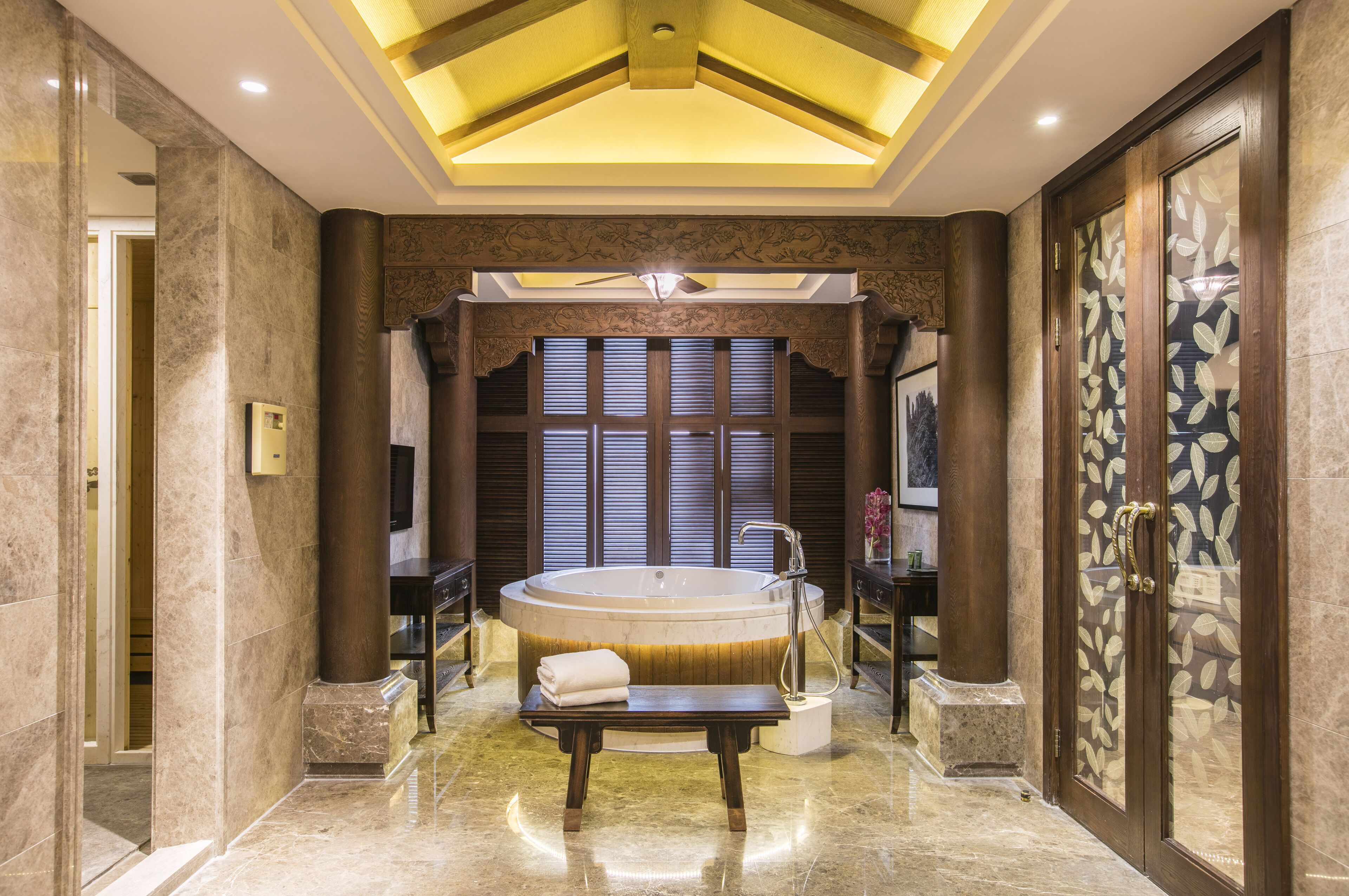 A luxurious bathroom with a large bathtub, marble flooring, and a bench with a towel.