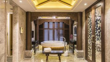 A luxurious bathroom with a large bathtub, marble flooring, and a bench with a towel.