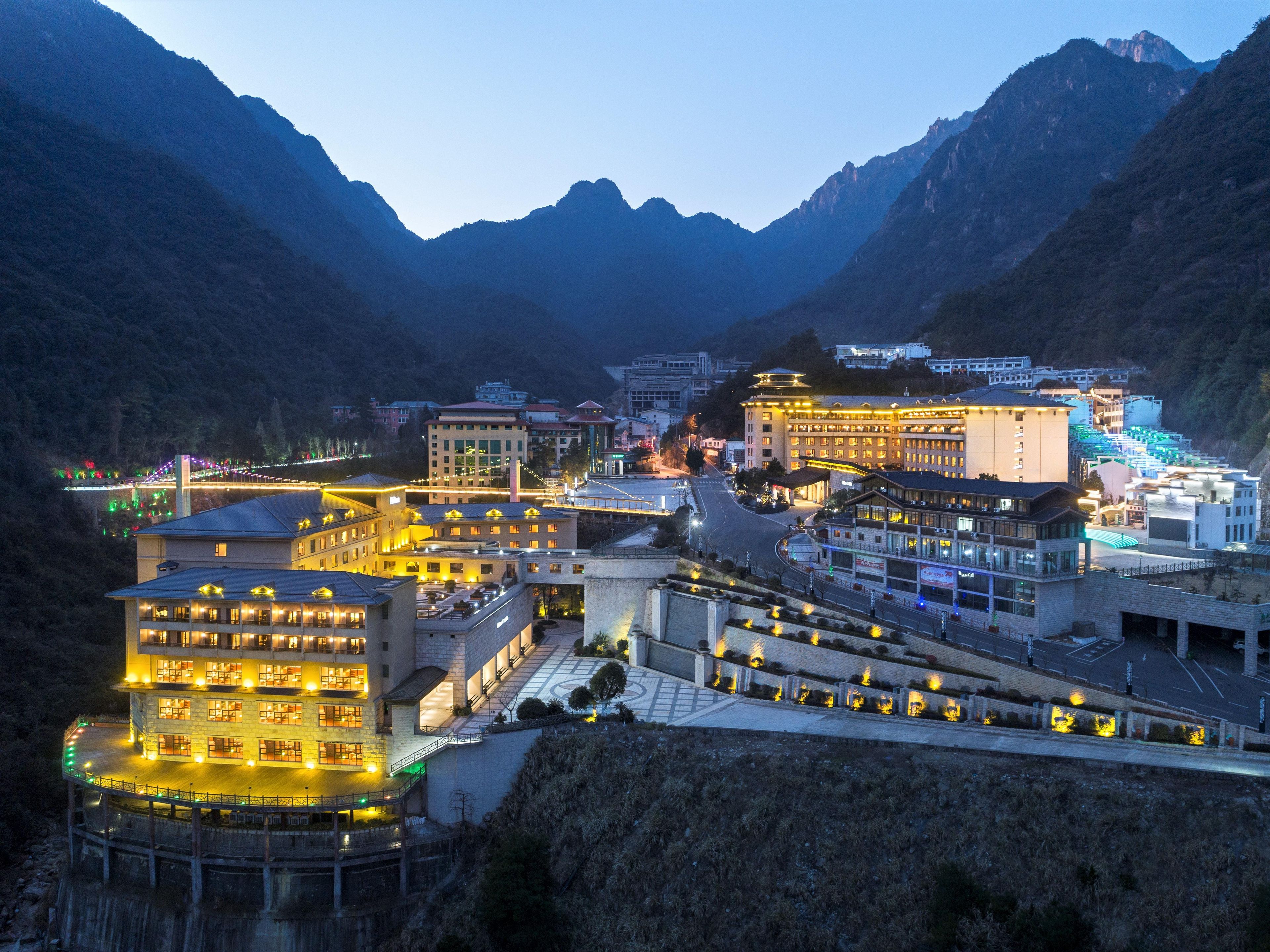 Un pueblo montañoso con edificios iluminados y un puente al fondo.