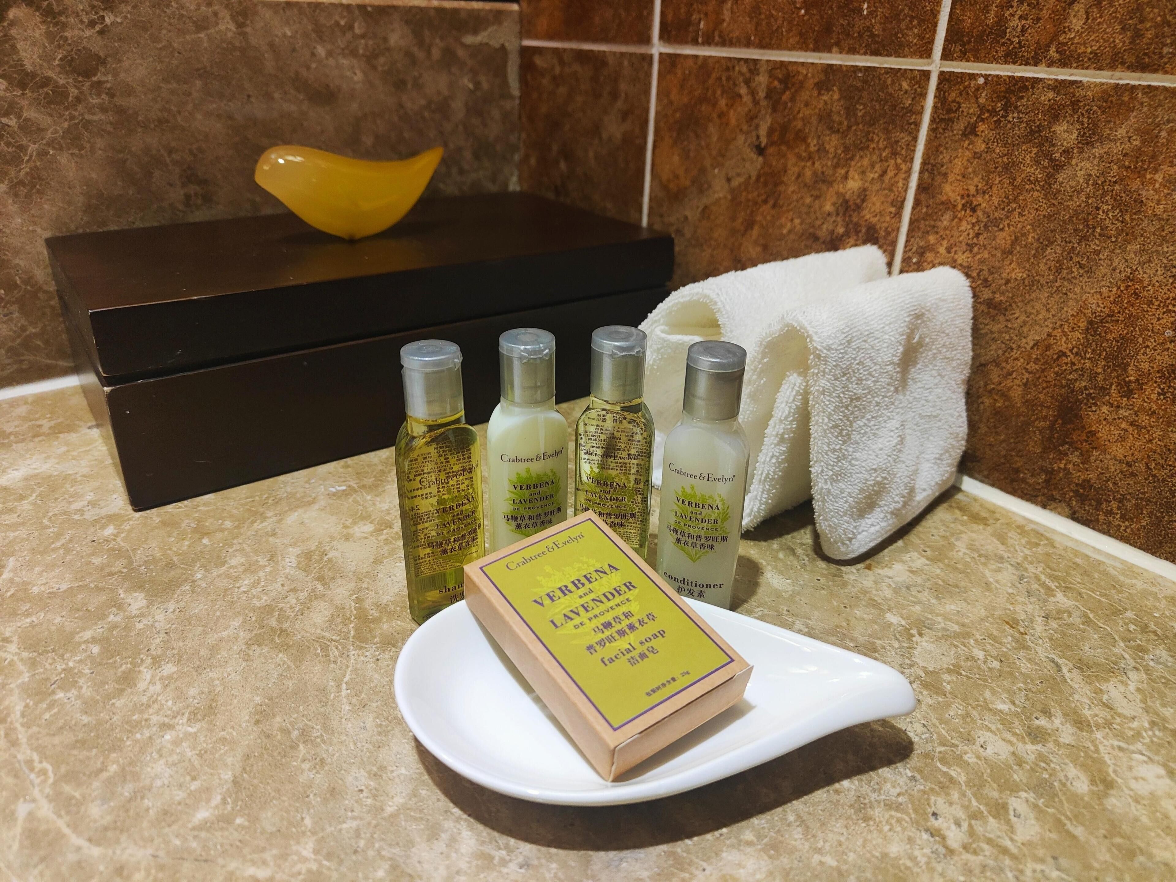 Una encimera de baño con un jabonero blanco, una pastilla de jabón amarilla y cuatro productos de lavanda Crabtree & Evelyn.
