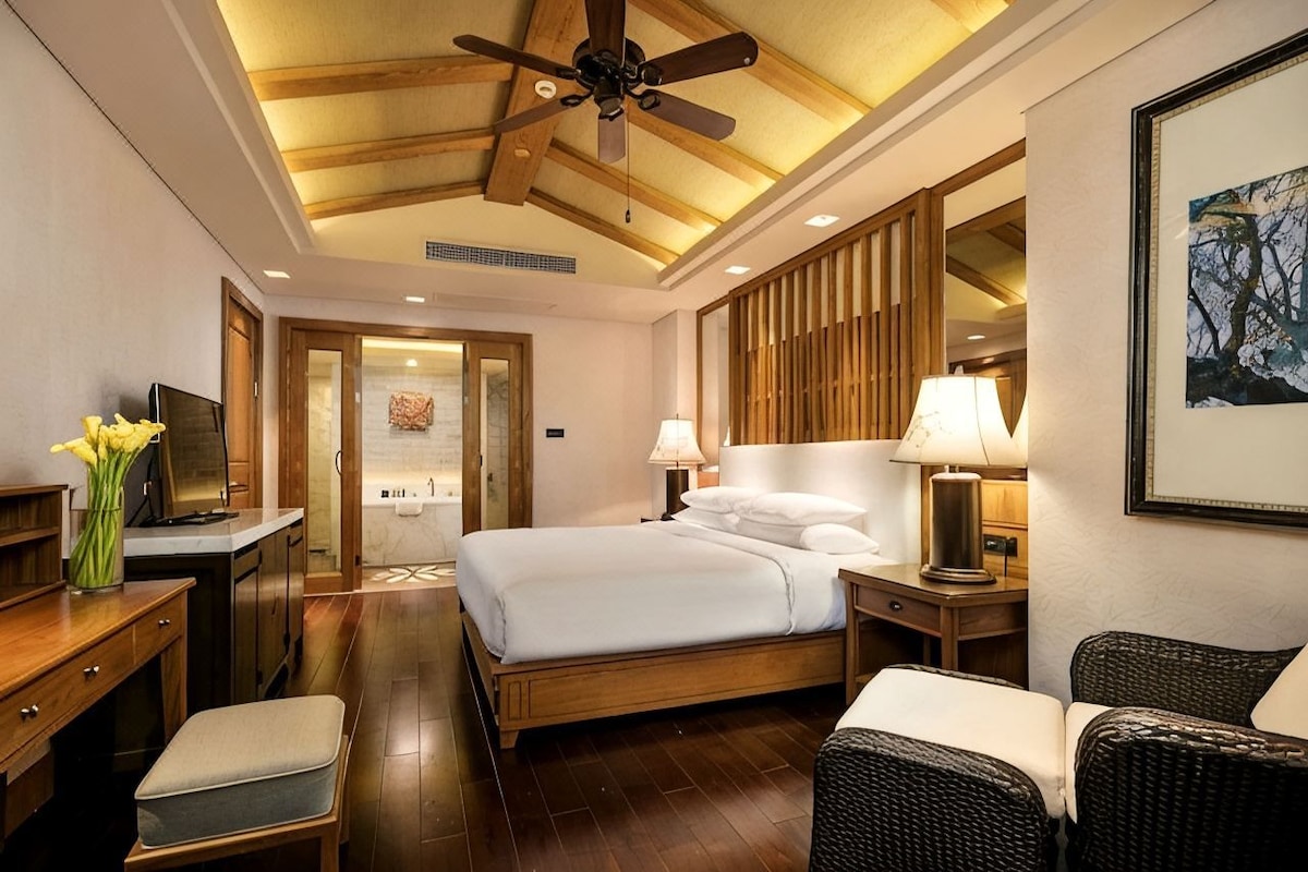 A hotel room with a bed, bedside tables, a desk, a chair, and a ceiling fan.