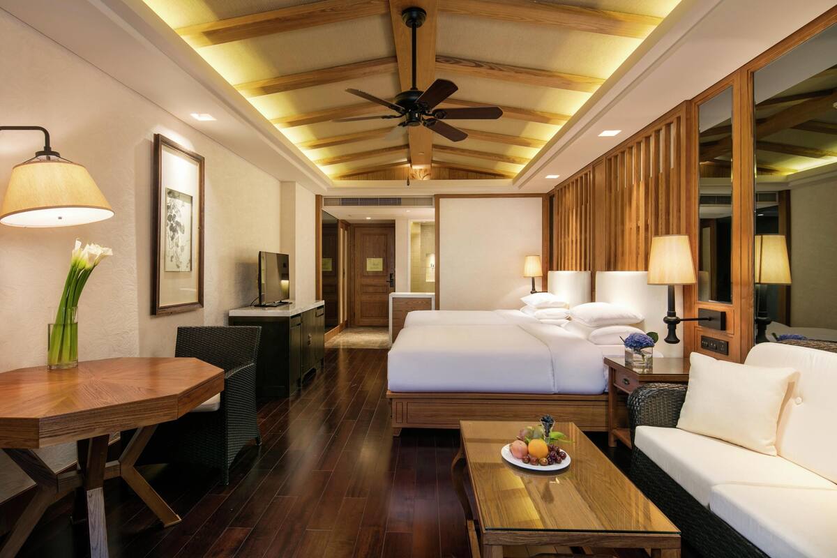 Habitación de hotel con cama, sofá, mesa de comedor, televisión y ventilador de techo.