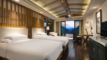A hotel room with two beds, a desk, a chair, a TV, and a view of mountains.