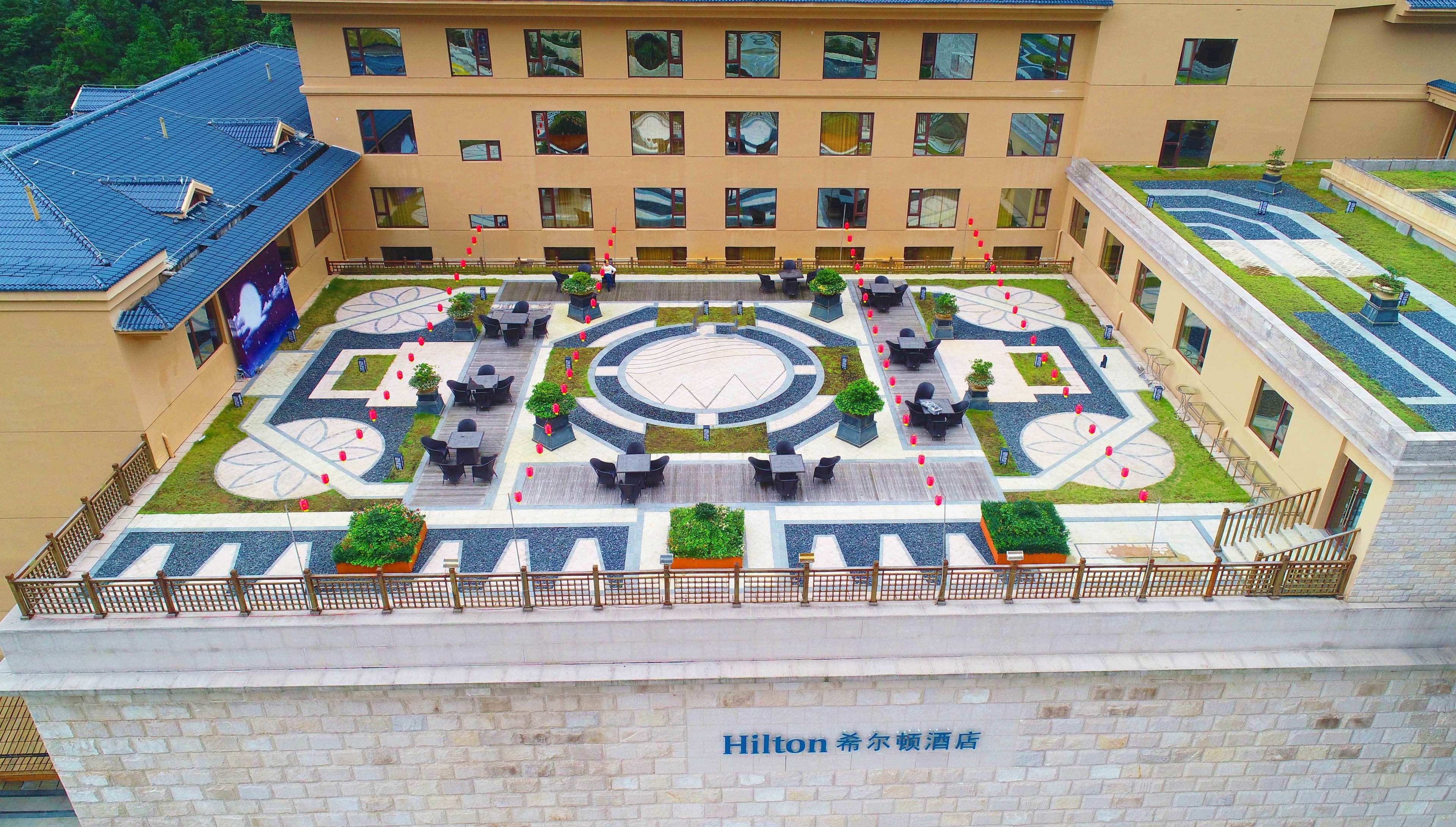 Pátio de hotel com área de estar ao ar livre, design circular central e placa indicando ser um hotel Hilton.