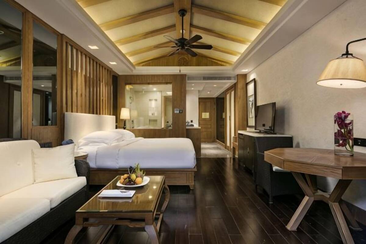 A hotel room with a bed, a sofa, a desk, a lamp, and a ceiling fan.