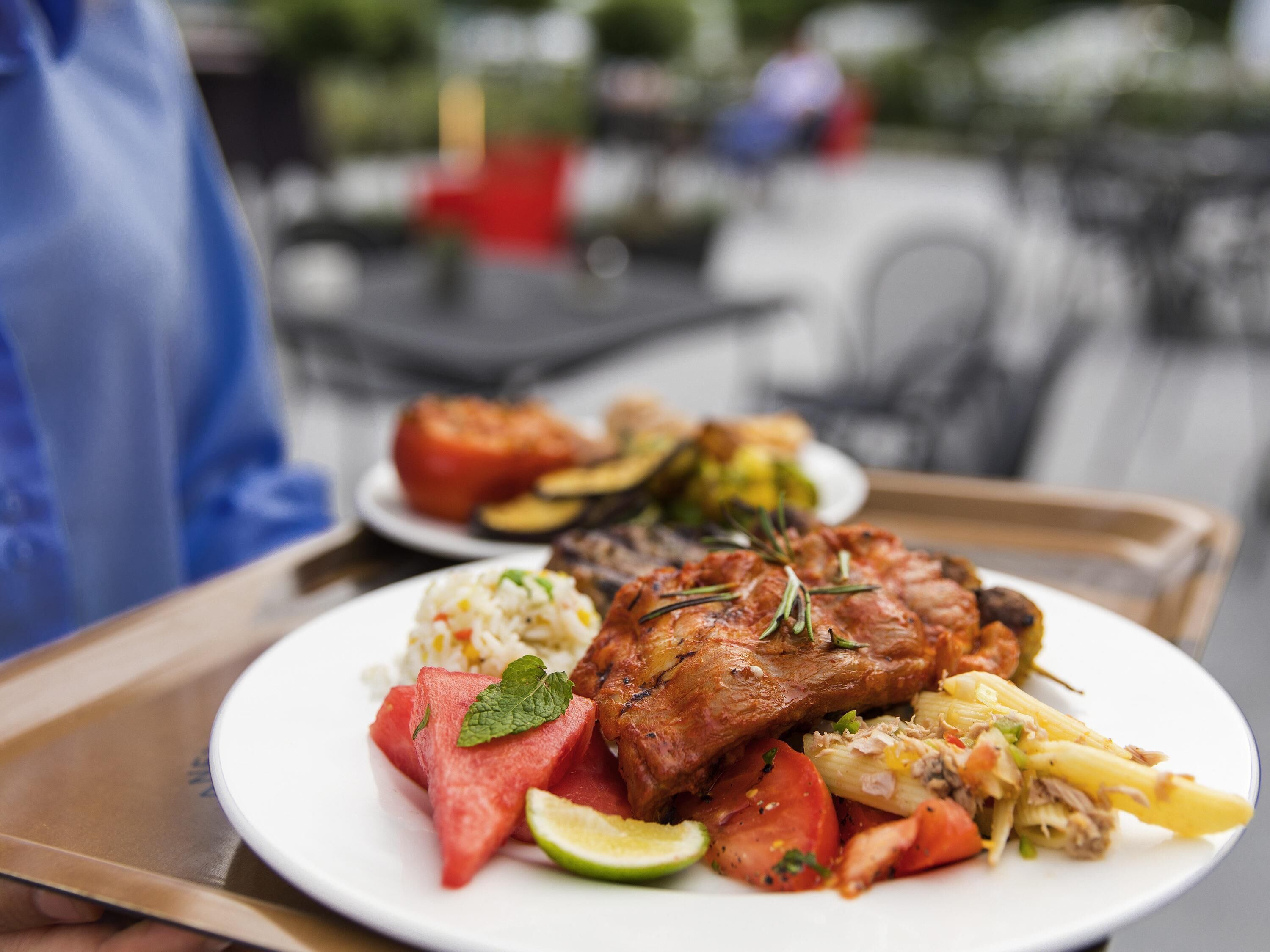 A tray with a plate of food including grilled meat, rice, vegetables, and a slice of watermelon.