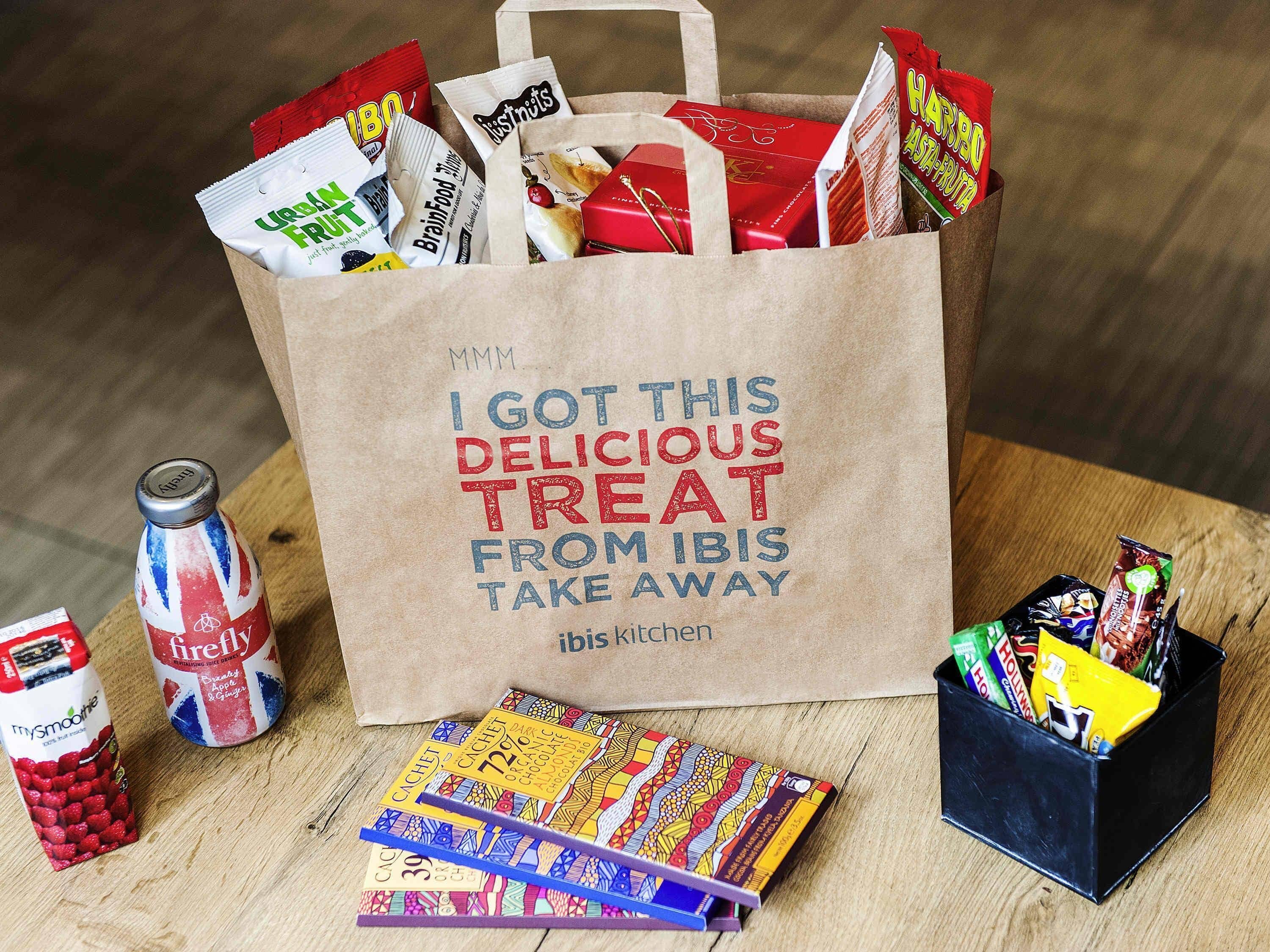 A paper bag filled with various snacks and a bottle of firefly drink, placed on a wooden surface.
