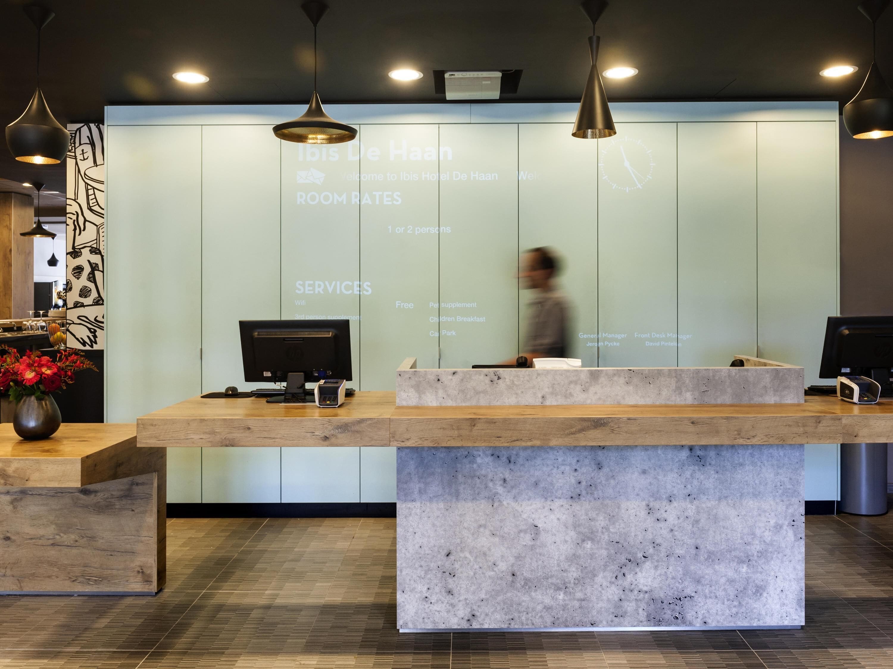 A hotel reception desk with a digital display of room rates and services, a wooden counter, and a modern interior design.