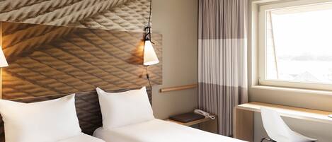 Una habitación de hotel con cama, escritorio, silla, teléfono y ventana con cortinas.