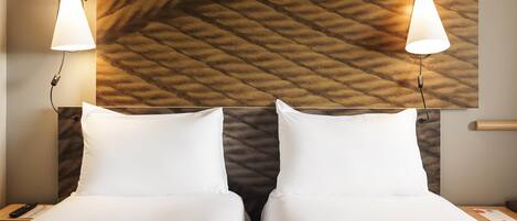 Habitación de hotel con dos camas, cabecera con diseño texturizado y dos lámparas de noche.