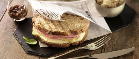 Ein Sandwich auf einer Schieferplatte, daneben eine Gabel und ein Messer.
