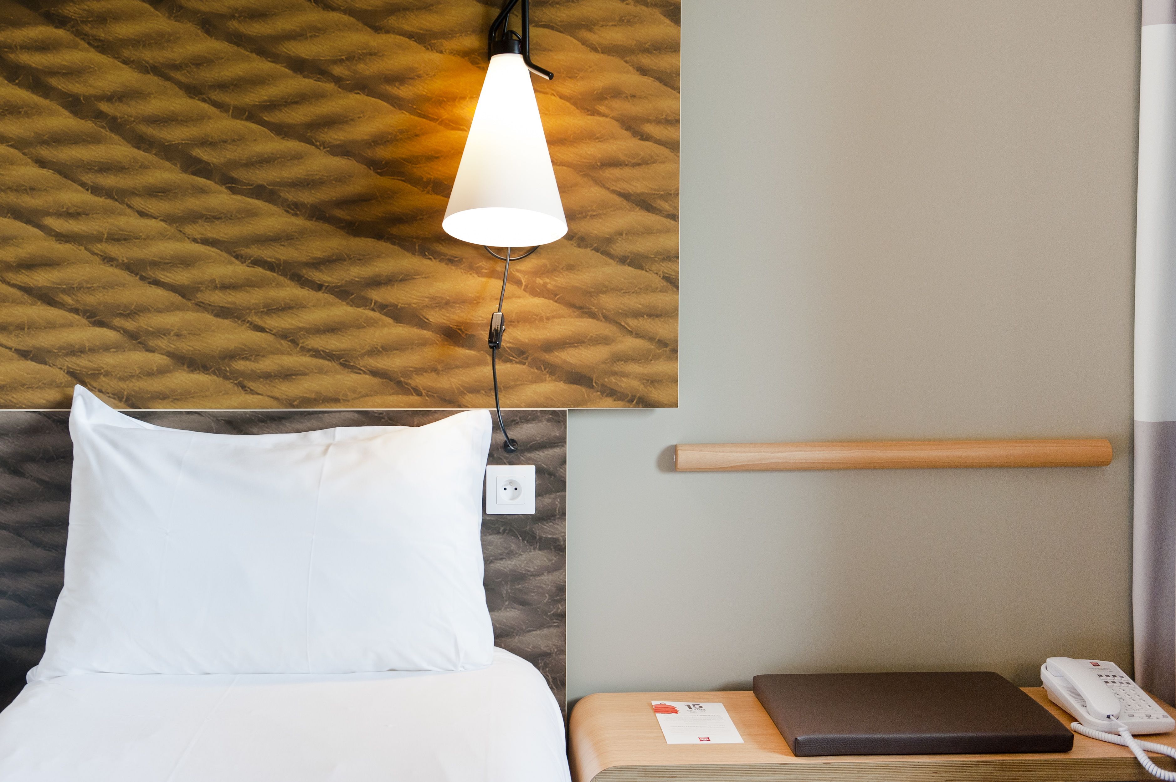 Una habitación de hotel con cama, mesita de noche con teléfono, lámpara y cabecero de madera.