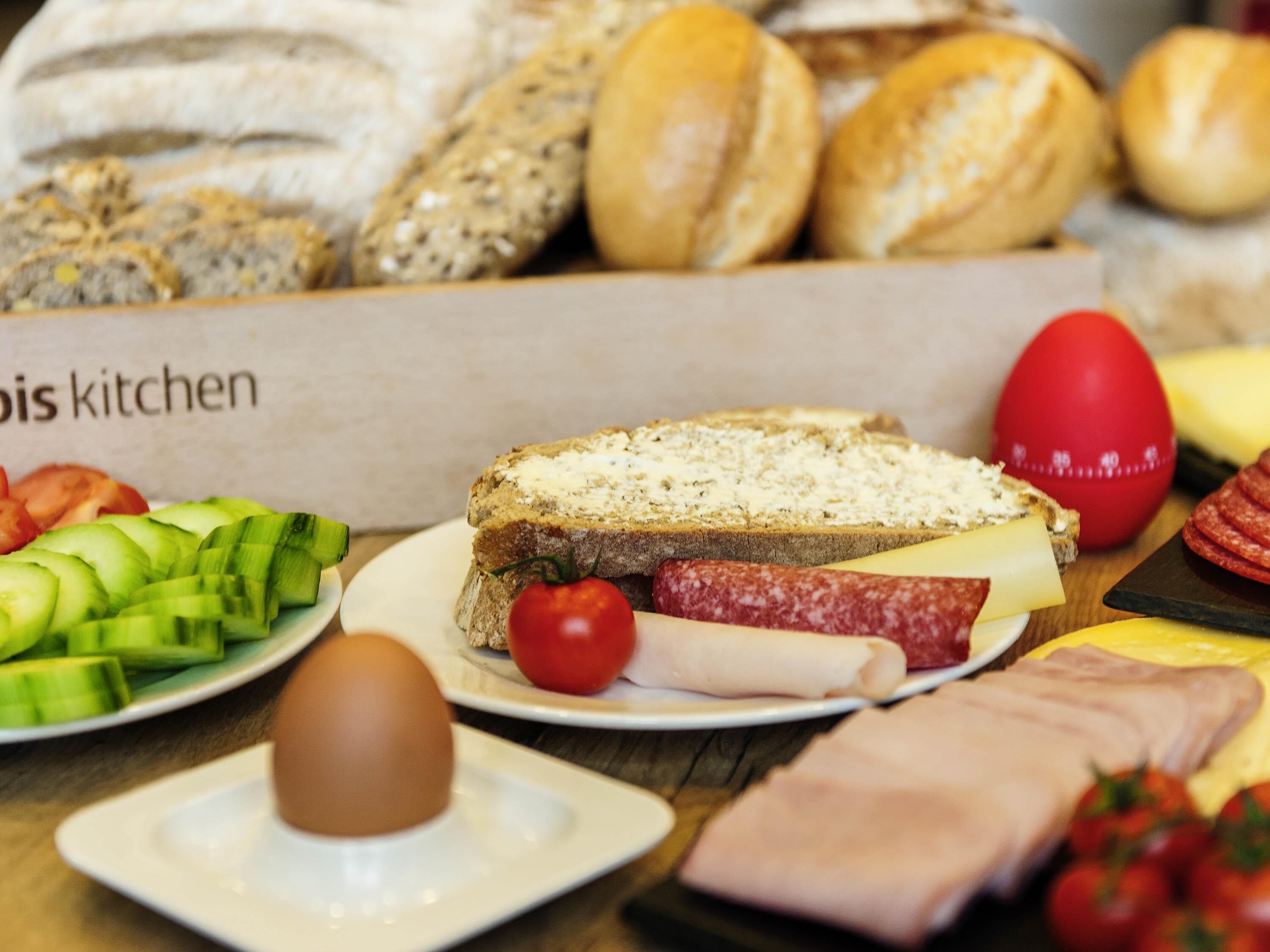 Eine Auswahl an Speisen, darunter Brot, Käse, Schinken und Gemüse, auf einem Tisch.