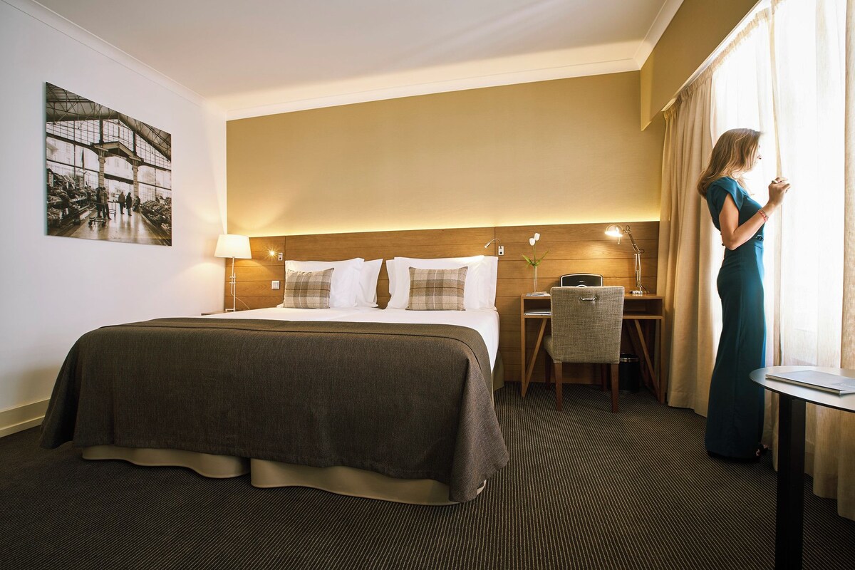 A hotel room with a large bed, a desk, and a chair.