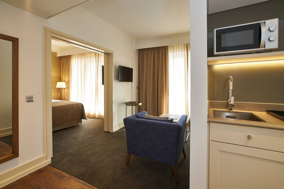A hotel room with a bed, a seating area, a TV, a microwave, and a sink.