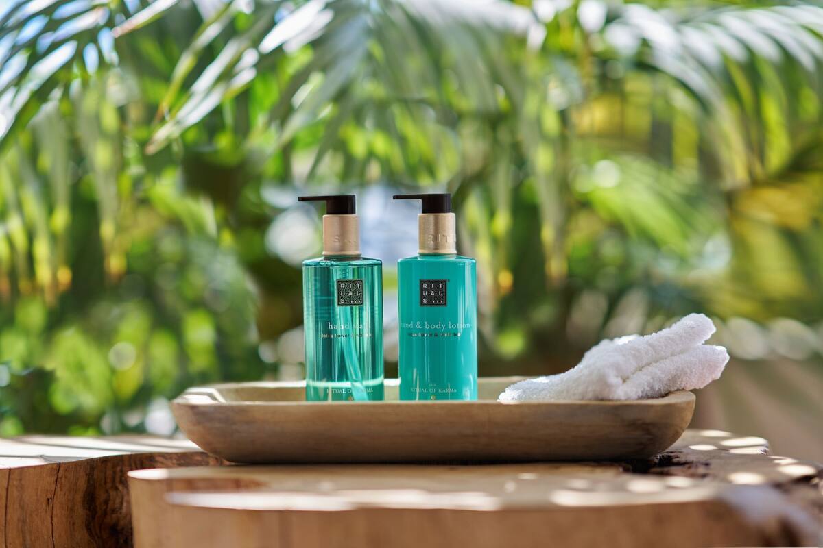 Two bottles of hand and body lotion on a wooden surface with a bowl of white towels.