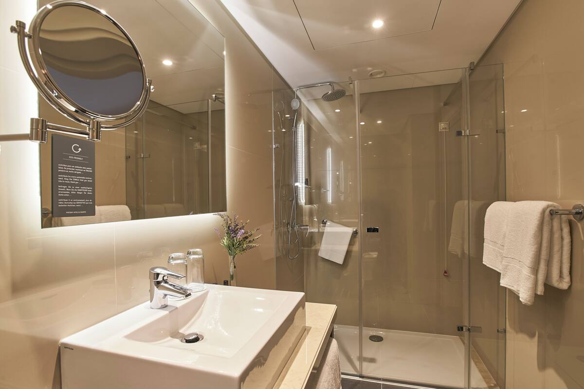 A modern bathroom with a glass-enclosed shower, a large mirror, and a white sink.