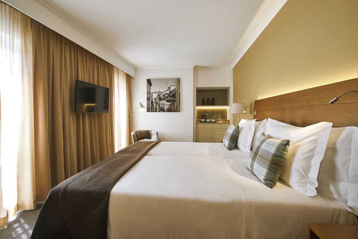 A hotel room with a large bed, a flat-screen TV mounted on the wall, a desk with a lamp, and a painting on the wall.