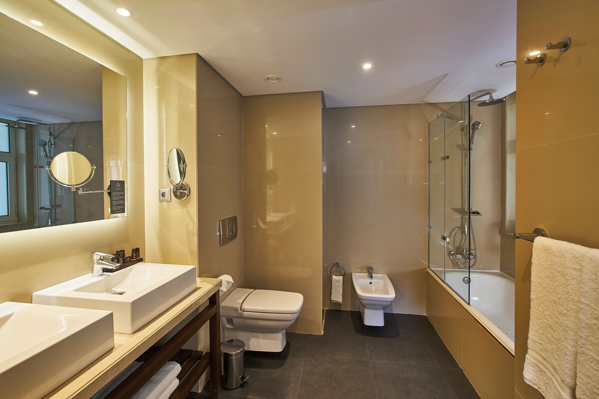 A modern bathroom with two sinks, a toilet, a bidet, a glass-enclosed shower, and a large mirror.