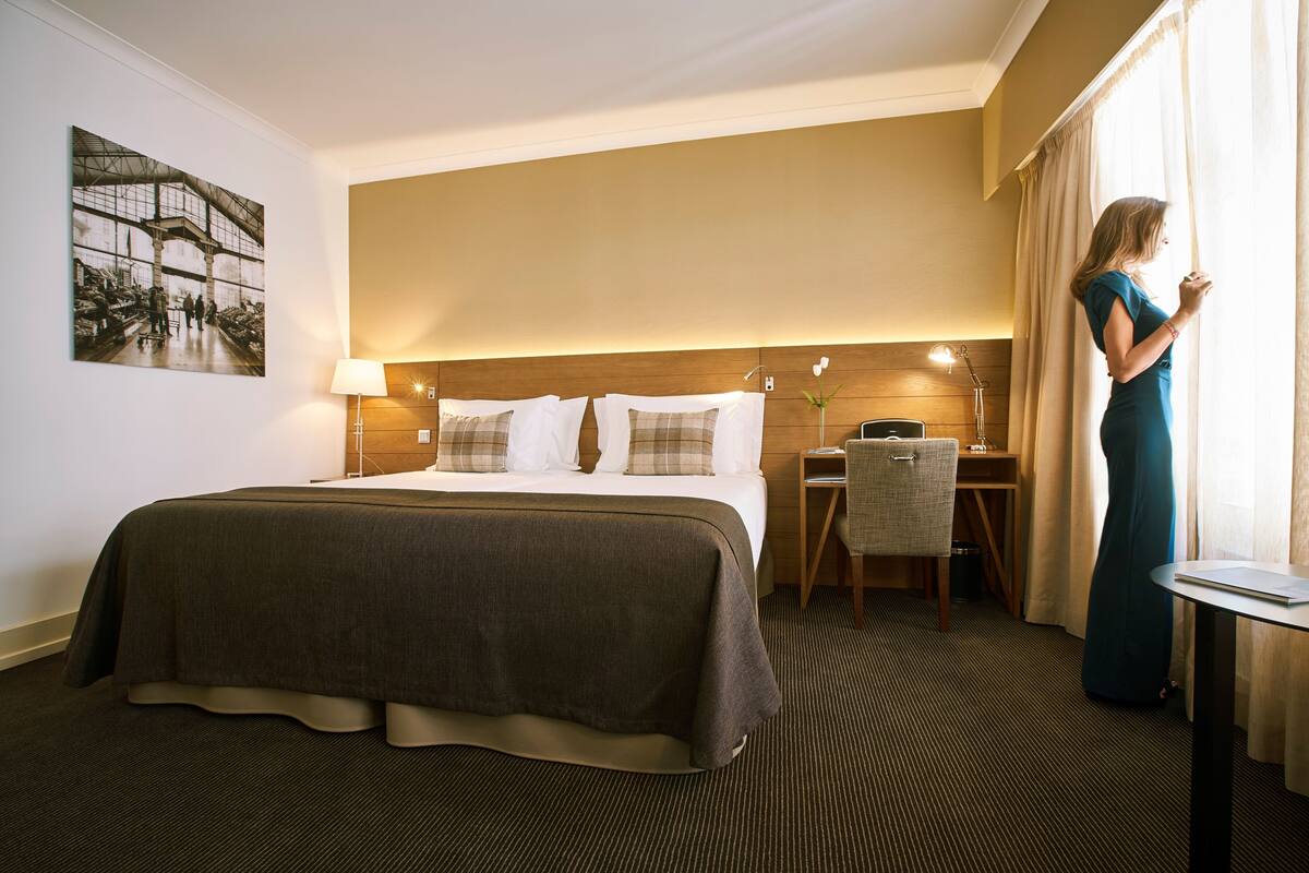 A hotel room with a large bed, a desk, a chair, and a window with curtains.