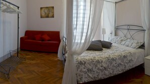 Un dormitorio con cama, un sofá rojo, un armario y una percha para ropa.