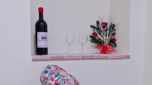Un taburete de madera pequeño con un cojín floral, una botella de vino y dos copas de vino sobre un estante encima de una escalera.