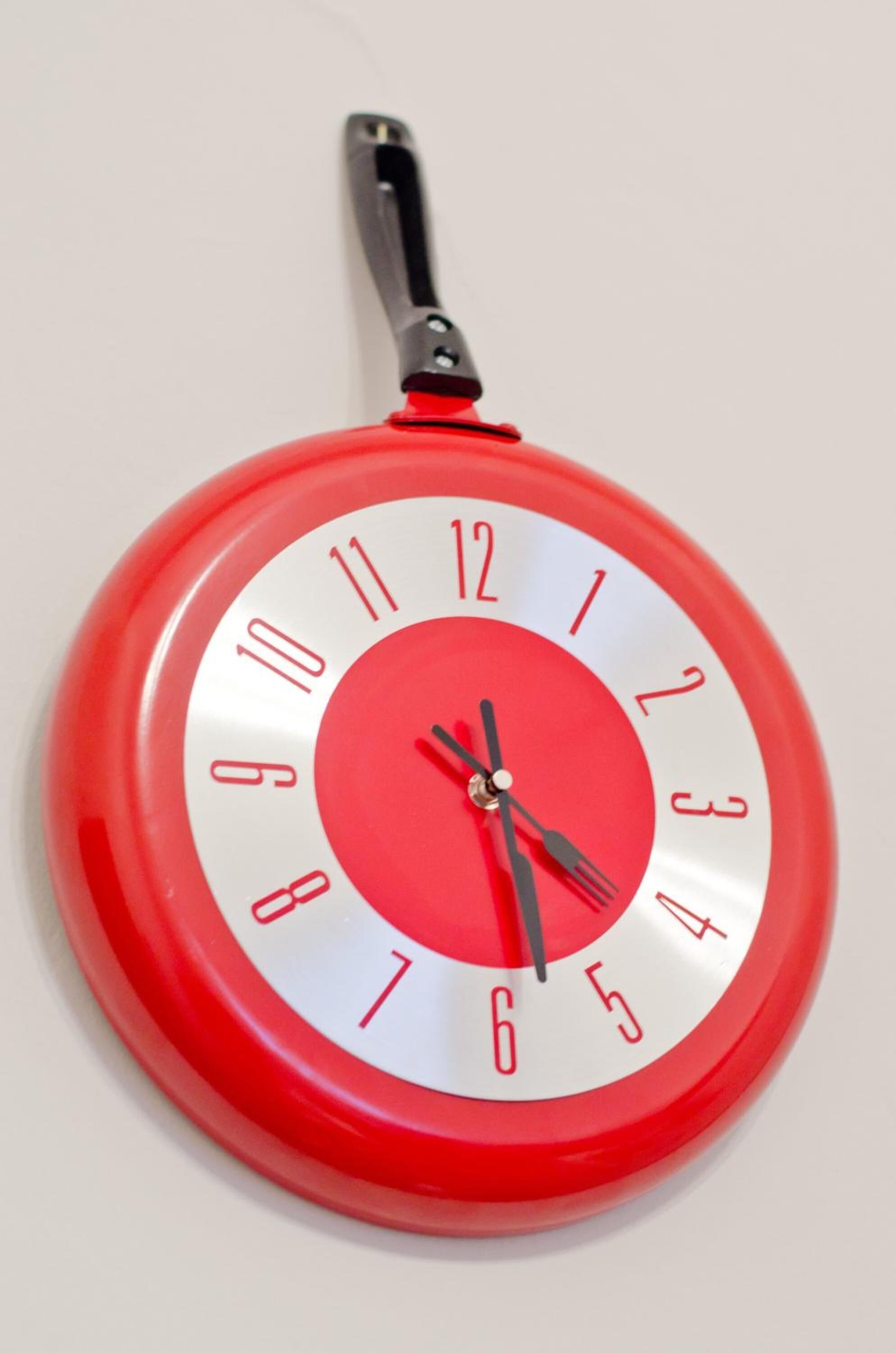 Une horloge murale rouge avec un manche noir.