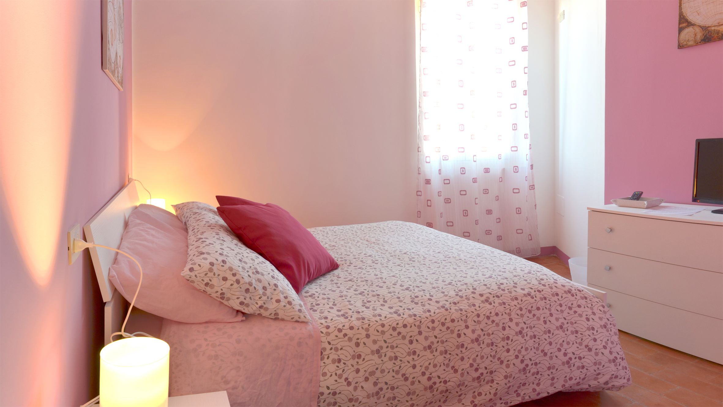 A bedroom with a bed, a bedside table, a lamp, and a window with curtains.