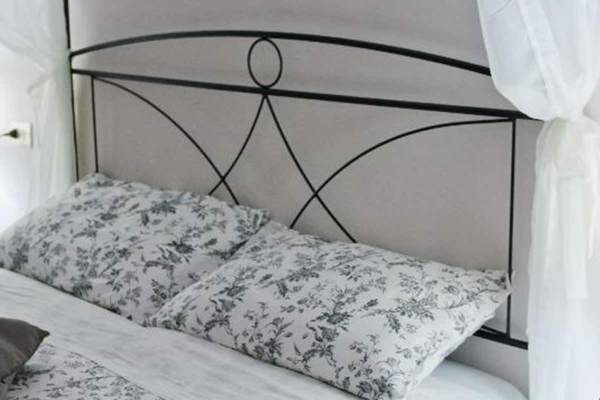 A bed with a metal headboard, white bedding, and a nightstand with a lamp.