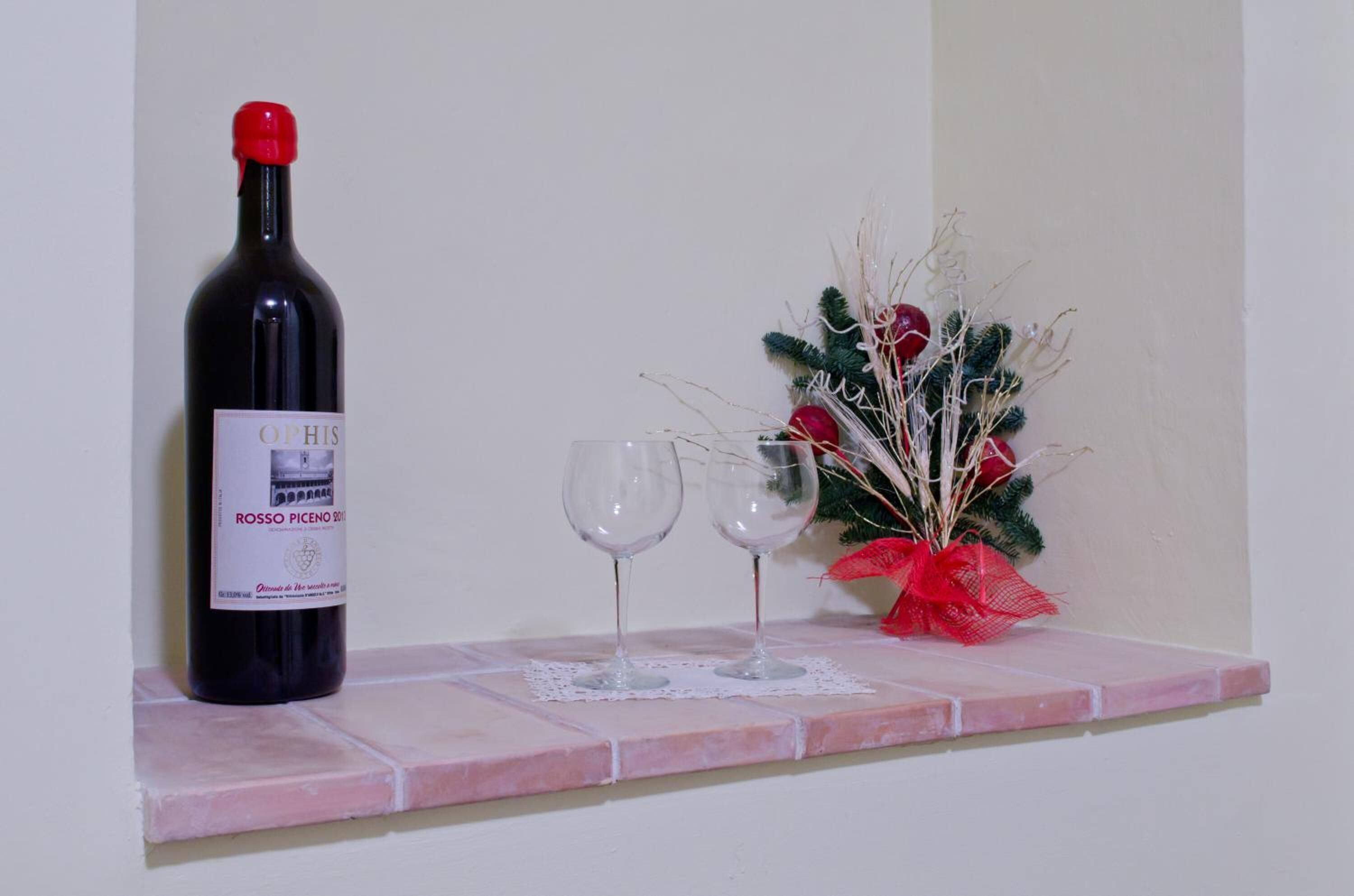 A bottle of rosso piceno wine on a shelf with two empty wine glasses and a small Christmas decoration.