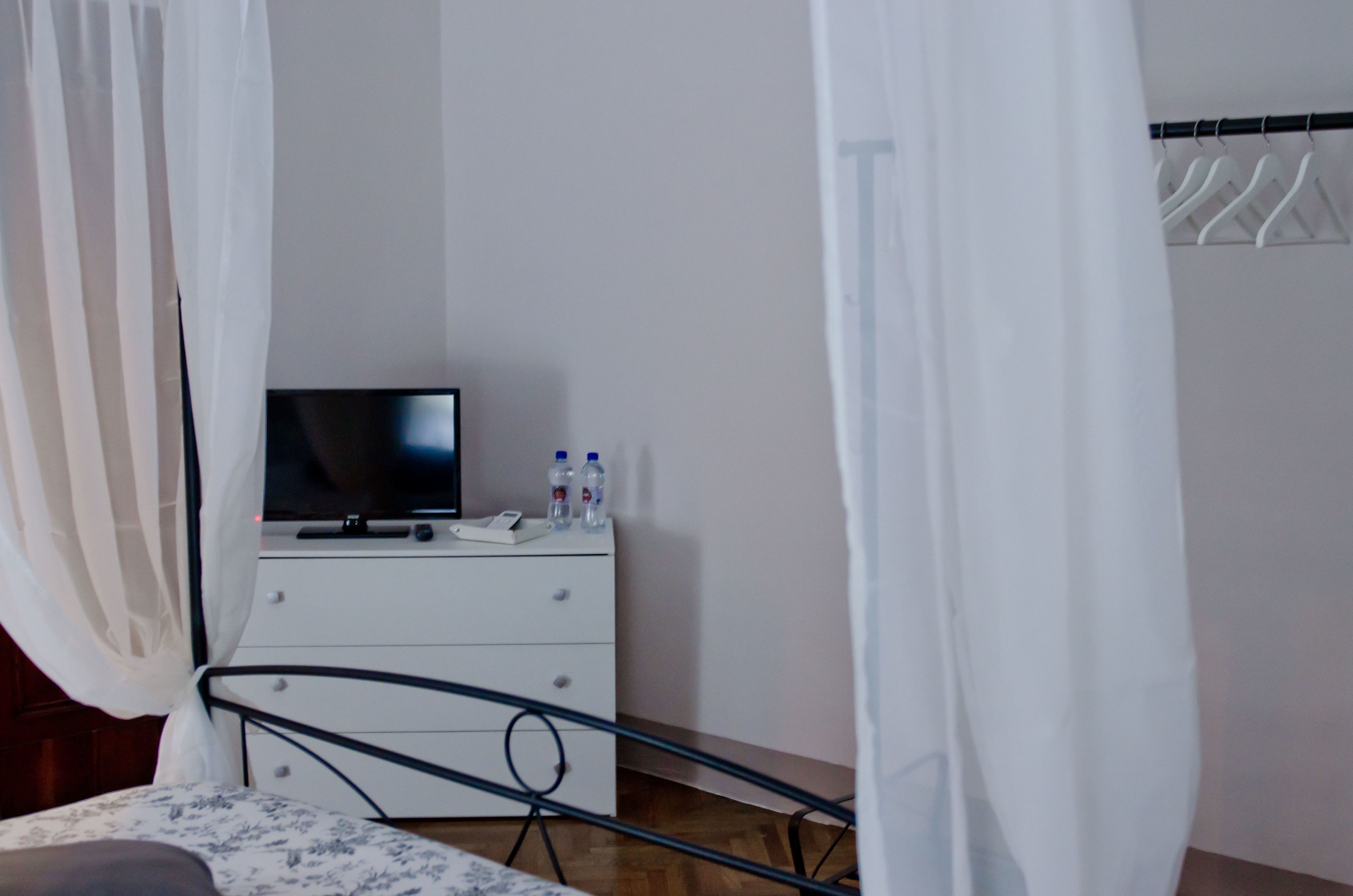 Une chambre à coucher comprenant un lit, une table de chevet avec un téléviseur, une commode blanche et une armoire.