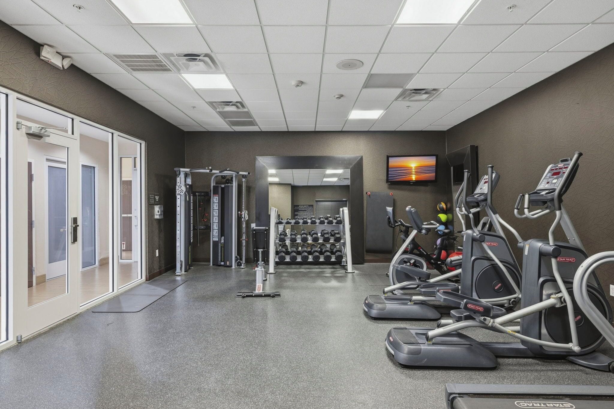 A gym with treadmills, elliptical machines, and a weight rack.