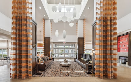 A spacious lobby with a patterned carpet, a central seating area, and a modern chandelier.